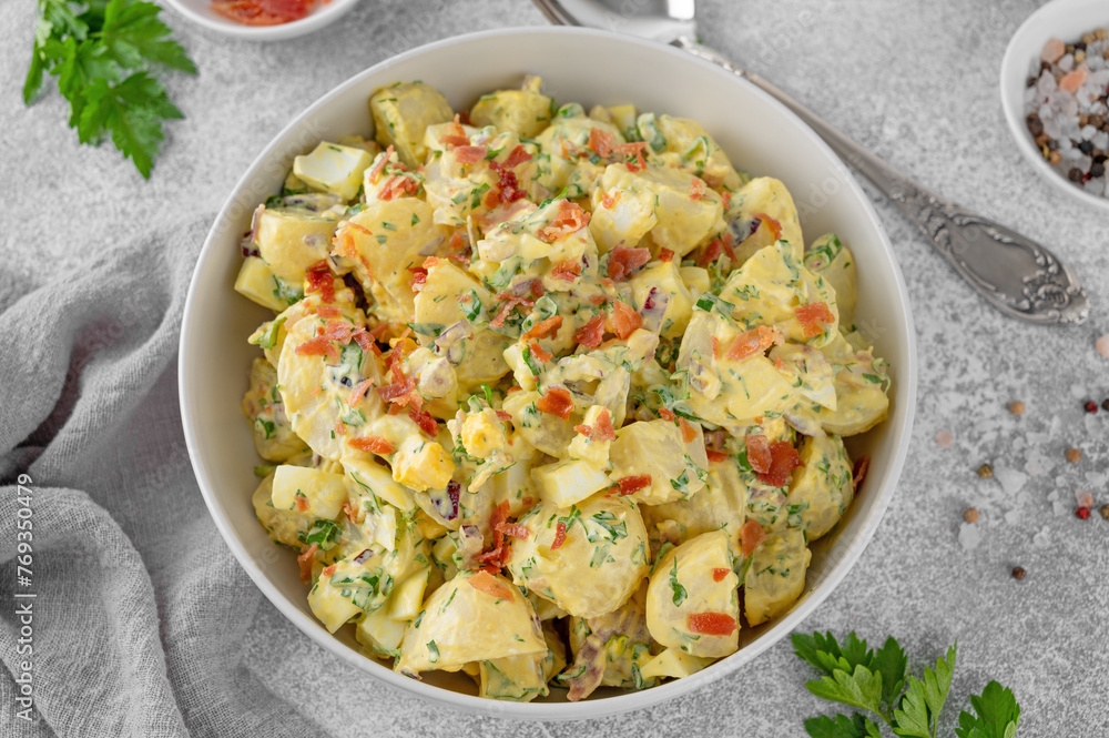 Salad of potatoes, eggs, bacon and fresh herbs with mayonnaise and yogurt dressing in a bowl on a gray concrete background. Salad of potatoes, eggs, bacon and fresh herbs with mayonnaise and yogurt dressing in a bowl on a gray concrete background.