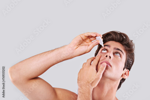 Man, allergies and treatment with eye drops for infection, sight or vision on a gray studio background. Male person or young model with pharmaceutical for optic hygiene, dry pupil or iris on mockup