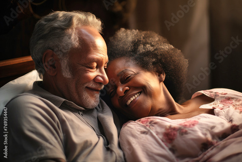 An elderly dark-skinned man and woman, a loving couple, are laying side by side together in bed