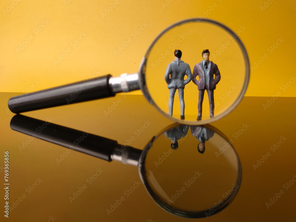 Miniature people and magnifying glass with reflection on a yellow background