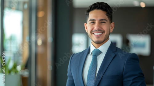 Smiling elegant confident young professional Latino hispanic business man , male proud leader, smart Latin businessman lawyer or company manager executive looking at camera standing in office