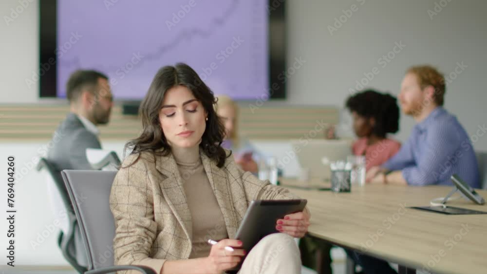 Young woman focused on her tablet with colleagues in the background. Young woman focused on her tablet with colleagues in the background.