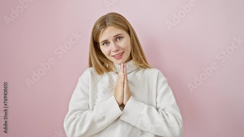 Confident beautiful blonde girl, standing praying fervently with hands together over pink isolated background, smiling as she hungrily asks for sweet forgiveness. photo