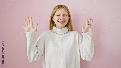 Happy blonde girl, caucusing her ten fingers, smiling and standing confidently over an isolated pink background demonstrating the idea of counting to ten photo