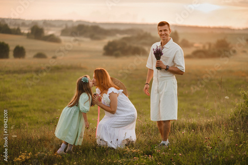 A beautiful happy family of three is standing in a field at sunset
