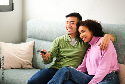 Multiethnic couple smile and watch TV, movie or film together on sofa. photo