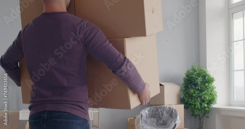 Young clumsy guy holding many cardboard boxes in hands losing his balance and falling on the floor in new apartment on moving day. Move, rent and relocation concept. 4k video. slow motion video.