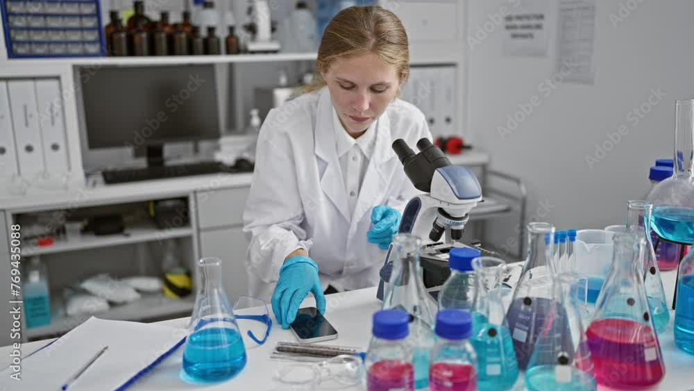 A focused woman researcher using a microscope and smartphone in a laboratory surrounded by colorful chemicals. A focused woman researcher using a microscope and smartphone in a laboratory surrounded by colorful chemicals.