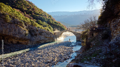 People crossing the Kadiut Bridge in Benje, Permet, Albania. Ancient stone bridge. Beautiful natural wonders. Holidays and leisure time. Fisherman fishing in the river. Natural thermal baths.