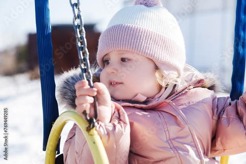 Beauty baby . Adorable girl having fun on a swing on beautiful autumn day . Portrait of cute girl playing in the winter park in sunny day