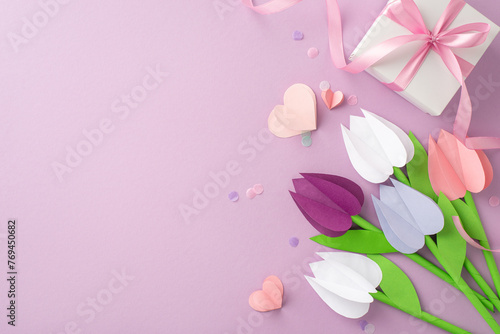 Handmade ode to motherhood. Overhead glimpse of paper tulips, a present tied with a ribbon, little hearts, and light confetti sprinkles on a pastel violet base, leaving margin for text