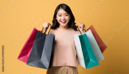 Portrait of Cheerful Asian woman holding shopping bags isolated over yellow background