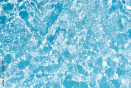 Bluewater waves on the surface ripples blurred. Defocus blurred transparent blue colored clear calm water surface texture with splash and bubbles. Water waves with shining pattern texture background.