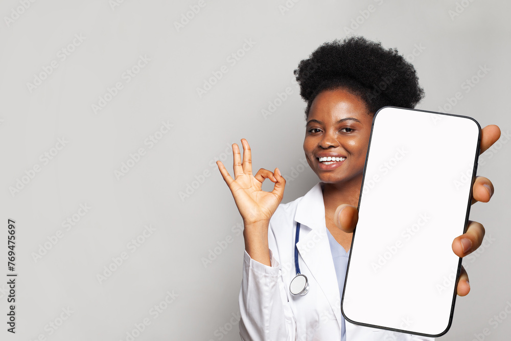 Happy doctor shows a phone with a blank display. Online medical consultation and medical healthcare and application. - obrazy, fototapety, plakaty 
