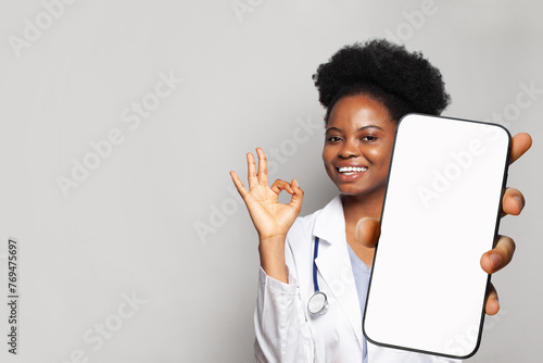 Happy doctor shows a phone with a blank display. Online medical consultation and medical healthcare and application. © millaf