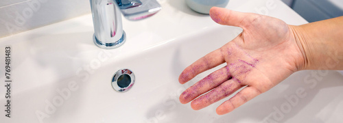 Close up of unrecognizable woman removing purple glitter of her hand into washbasin at bathroom. Water pollution by microplastics composition concept.