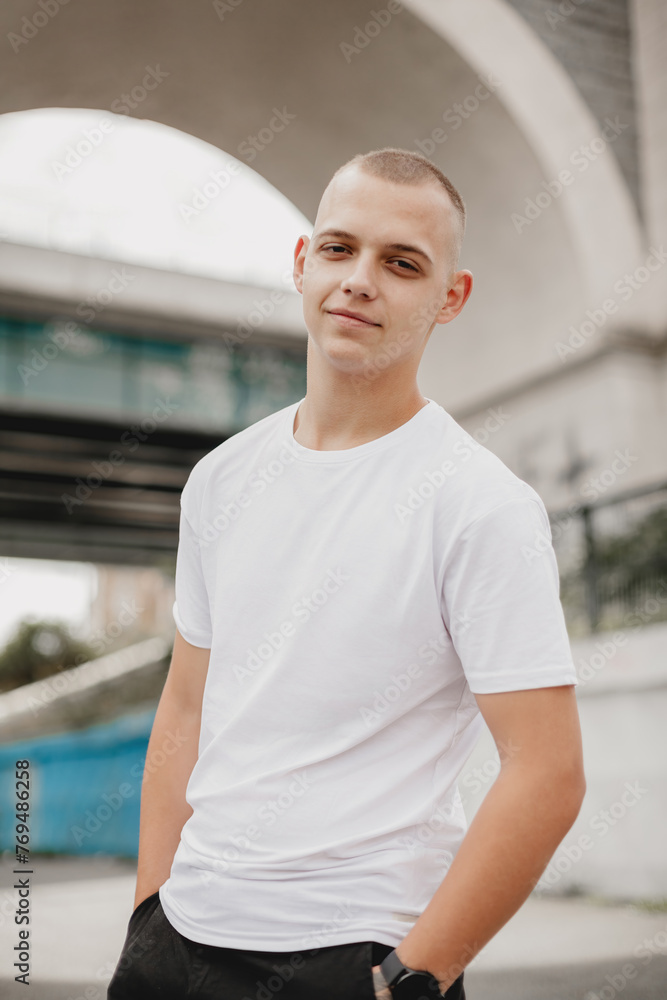 A young man wearing a white shirt stands in front of a bridge. He is smiling and looking at the camera A young man wearing a white shirt stands in front of a bridge. He is smiling and looking at the camera