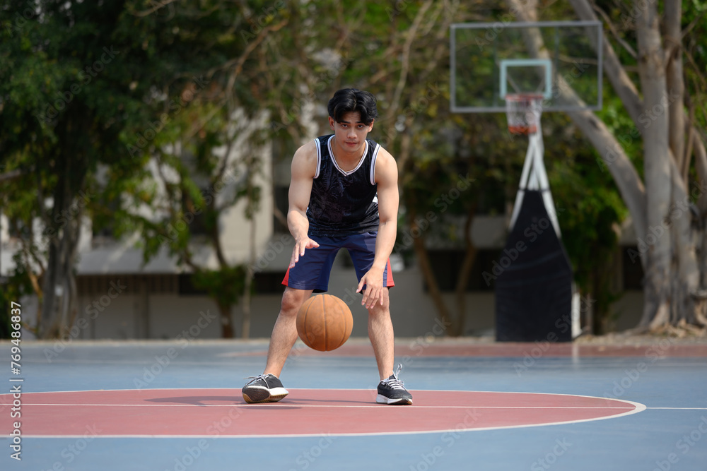 Young muscular basketball player dribbling a ball on an outdoor court