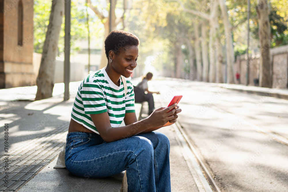 Happy African girl using yellow red phone outdoors at University campus. Smiling young woman having fun with online app Happy African girl using yellow red phone outdoors at University campus. Smiling young woman having fun with online app
