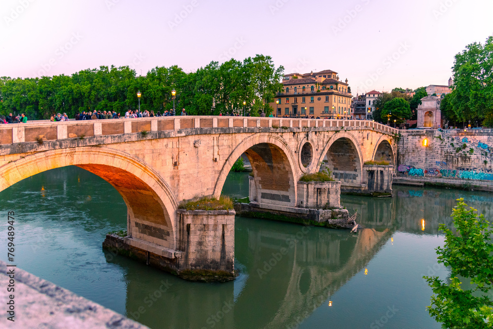 The sun casts a warm glow on the Ponte Sisto bridge, enhancing the historic charm of this ancient Roman bridge, while locals and tourists enjoy the serene riverscape. Rome, Italy