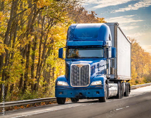Bonnet blue big rig semi truck tractor carry cargo semi trailer driving on the autumn highway road with forest on the side © OceanProd