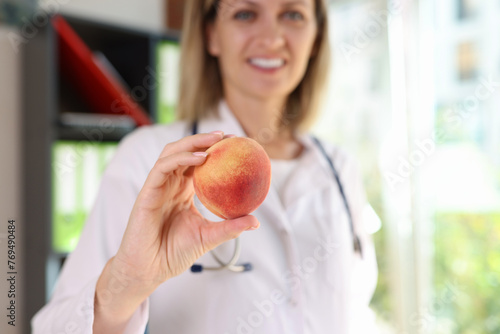 Smiling female nutritionist holds fresh peach fruit in her hand close-up.