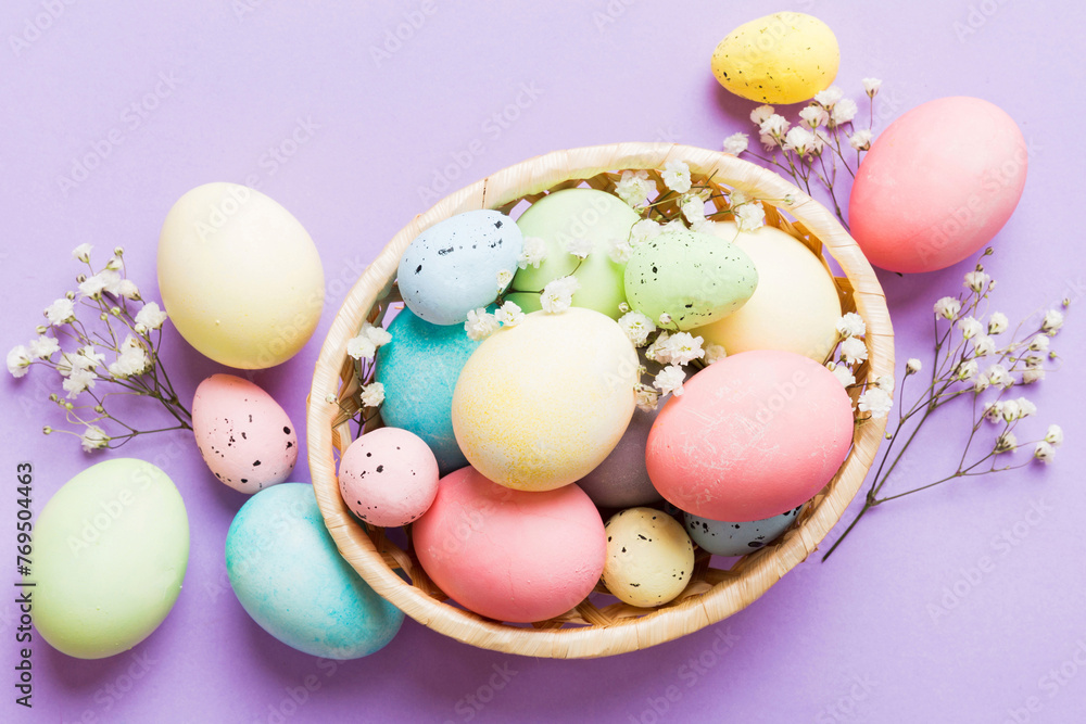 Fototapeta premium Happy Easter composition. Easter eggs in basket on colored table with gypsophila. Natural dyed colorful eggs background top view with copy space