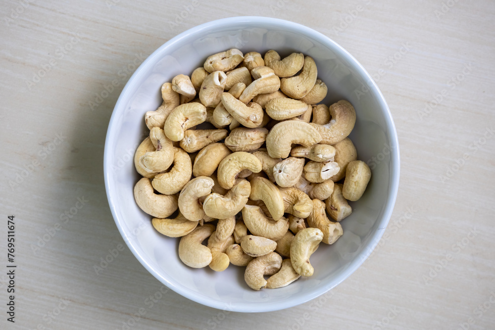 Healthy cashew nuts in a white bowl on a wooden background. Its scientific name is Anacardium occidentale and In the Bengali language, it is called Kaju Badam. Top view. Healthy cashew nuts in a white bowl on a wooden background. Its scientific name is Anacardium occidentale and In the Bengali language, it is called Kaju Badam. Top view.