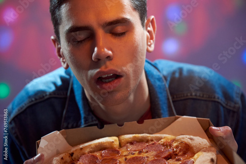 A young guy student sniffs fresh paperoni pizza in a cardboard box