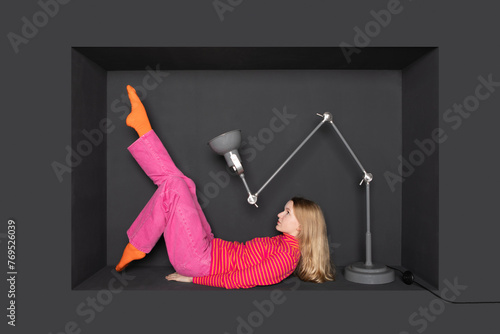Teenage girl lying in front of electric lamp by black background