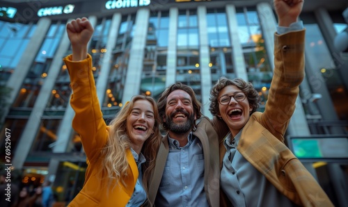 Energetic Business People Celebrating Outdoor Success. Three exuberant professionals raise their fists in the air in triumph outside a modern business building.