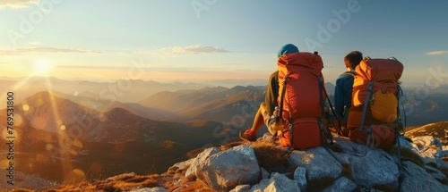 Hikers with backpacks relax on top of a mountain at sunset and enjoy the view of a valley