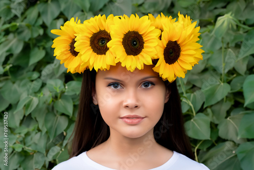 girl with a wreath. a stylish young girl with long black hair and a white T-shirt stands with a wreath of sunflowers on her head against a background of green trees, nature concept