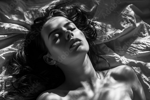 A woman is laying on a bed with her hair down. She is not wearing any clothes. The image has a mood of relaxation and comfort