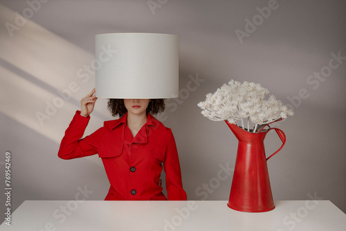 Frau im roten Mantel mit Lampenschirm am Kopf