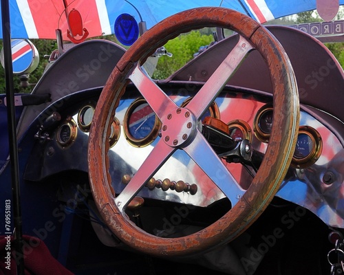 A wooden steering wheel and interior dashboard of a classic teal bugatti vintage car at a car show