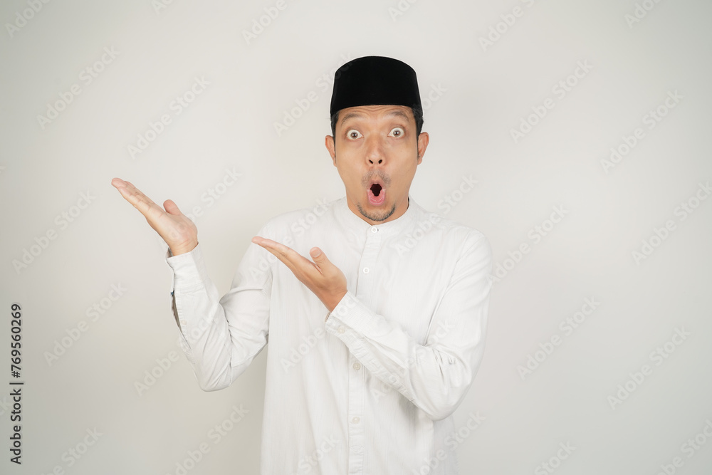 Wow face shocked expression Asian Muslim man wearing Arab costume pointing hand finger at empty space on isolated background - obrazy, fototapety, plakaty 