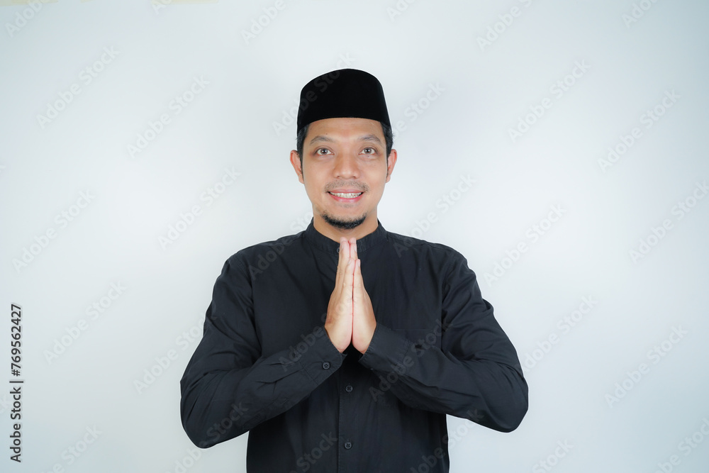 Happy smiling Asian Muslim man standing with Eid greeting gesture and welcoming Ramadan isolated background - obrazy, fototapety, plakaty 