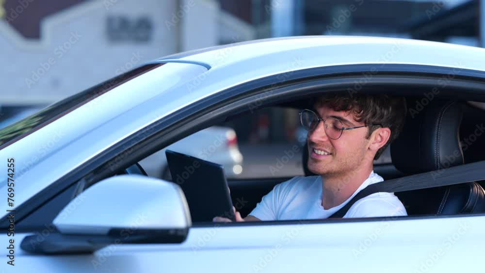 Smiling young man in glasses sitting in the car, using seat belt while working and holding digital tablet. Transport, job, technology and lifestyle concept. Slow motion Smiling young man in glasses sitting in the car, using seat belt while working and holding digital tablet. Transport, job, technology and lifestyle concept. Slow motion