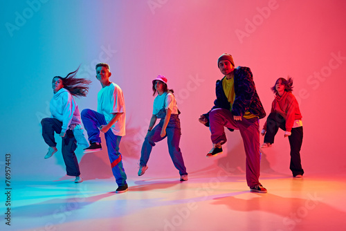 Group of talented dancers practices choreographed number in neon light against gradient colorful studio background. Concept of hobby, sport, fashion and style, action, youth culture, music and dance.