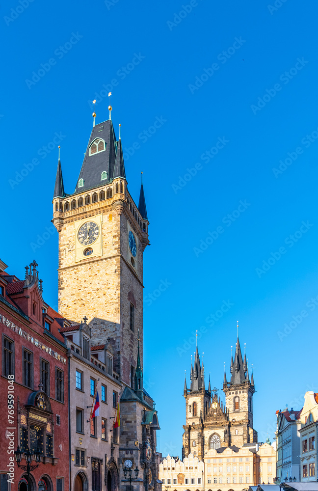 The historic clock tower stands tall against a clear blue sky in Prague Old Town Square, with other Gothic architecture visible in the background. Prague, Czechia