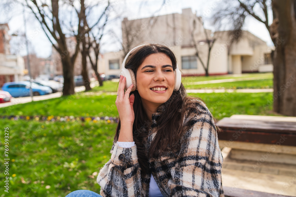 Fototapeta premium One young girl or woman is listening to music on her wireless headphones and enjoying the sun outdoors