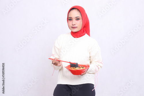 Asian woman wearing a hijab carrying chopsticks and a bowl containing ramen (Chinese food). Beautiful Muslim women are used for culinary, food and advertising content