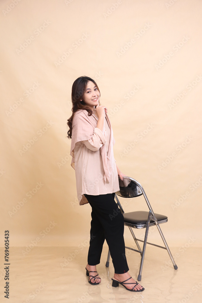 full body indonesia woman semi-hijab standing next to chair smiling, hands holding chair and chin. beautiful Muslim women for advertising, fashion, religion full body indonesia woman semi-hijab standing next to chair smiling, hands holding chair and chin. beautiful Muslim women for advertising, fashion, religion