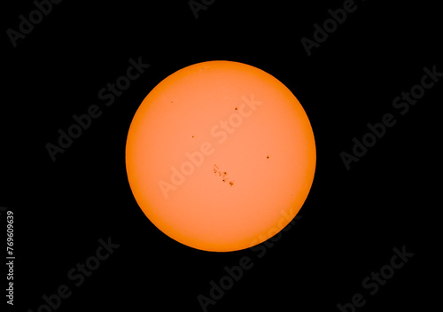 The orange coloured afternoon sun glowing with many sunspots using a homemade solar filter against a black background. March 24, 2014