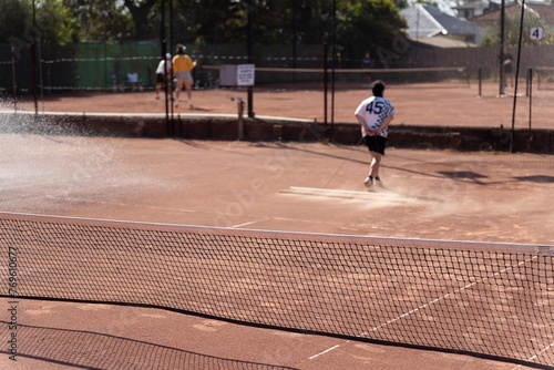 friends playing tennis on a clay court, watering and bagging a clay court. doing tennis court maintence photo