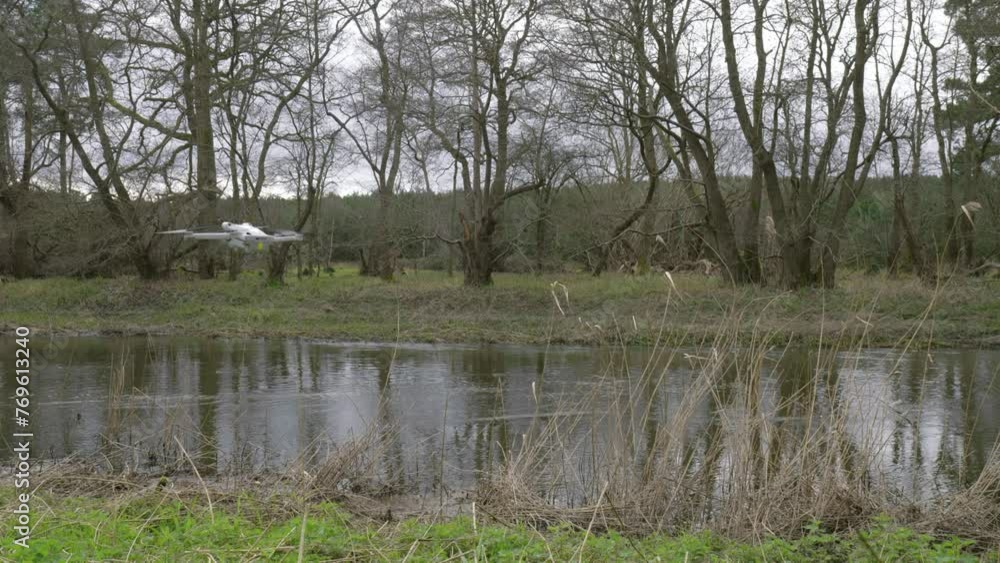 Drone flying down on the left side and disappearing towards the right side of the frame, in front of a river at Thetford forest camping ground, in Brandon, United Kingdom. Drone flying down on the left side and disappearing towards the right side of the frame, in front of a river at Thetford forest camping ground, in Brandon, United Kingdom.