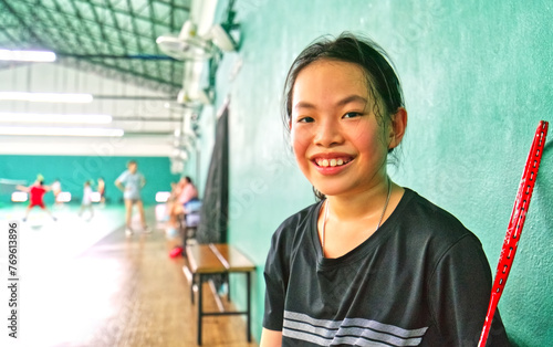 Portrait of Asian child girl at Badminton gym, eyes looking at camera and smiling, blurred environment of the gym, space for copy, landscape image.