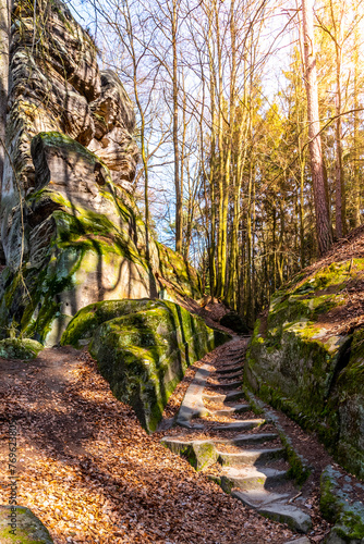 A serene path with stone steps meanders through towering sandstone formations, bathed in sunlight, amidst the verdant forests of Bohemian Paradise in the Czech Republic. photo