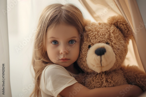 A shy preschool girl hiding behind a teddy bear. A little girl hugging a teddy bear close up to the camera
 photo